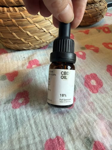 Bottiglia di CBD Oil 18% Full Spectrum 10ml Slow Weed su tovaglia con stampa di rose