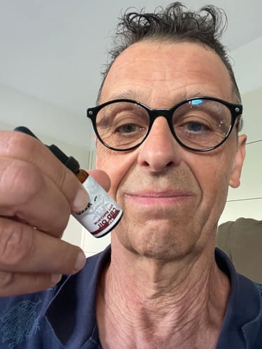 Uomo con occhiali sorridente che mostra una bottiglia di Olio CBD Slow Weed