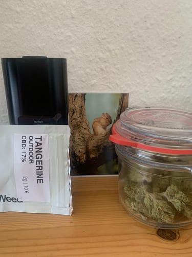 Busta Slow Weed Tangerine Outdoor accanto a un vasetto di vetro con i fiori CBD